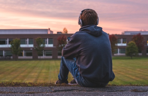 Older student listening to headphones on a school field at sunset.